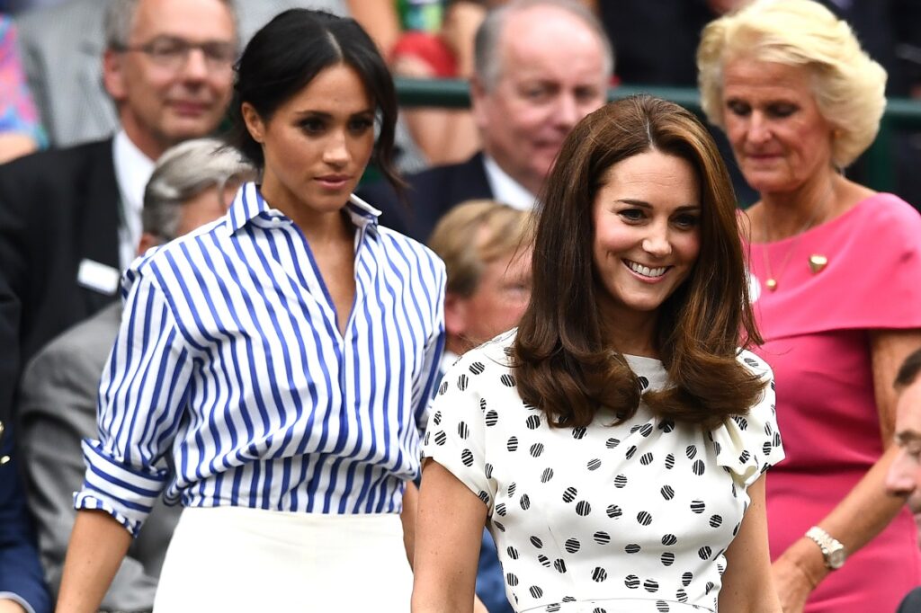 Kate Middleton purtând o rochie albă cu buline negre alături de Meghan Markle care poartă o bluză albastră cu dungi albe în timp ce se află la Wimbledon 2018