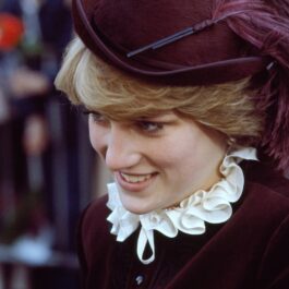 Portret al Prințesei Diana în timp ce poartă o pălărie și un costum violet și zâmbește publicului