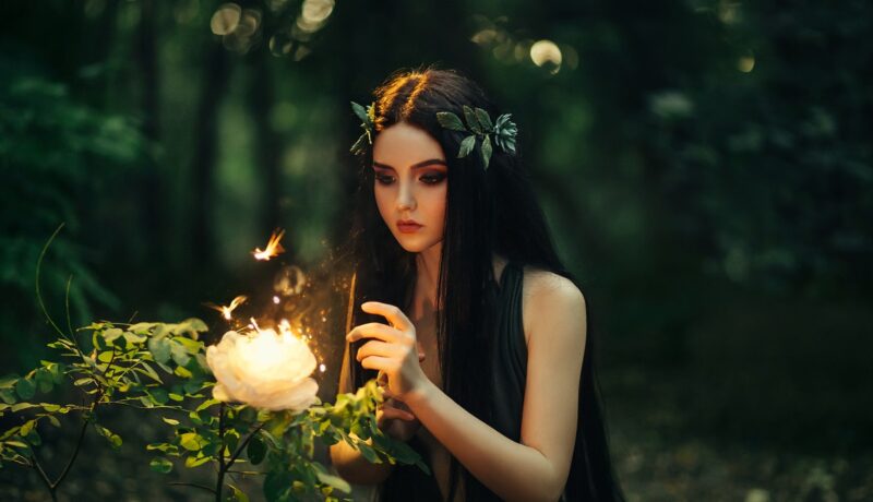 Un cadru feeric cu o pădure verde întunecată și o zână în timp ce privește un trandafir luminat pentru că este una dintre cele mai norocoase zodii ale lunii august 2021