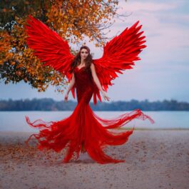 Un cadru feeric din fața unui lac unde se află o femeie superbă cu rochie roșie și aripi de înger roșii pentru a demonstra că este una dintre cele mai pasionale femei din zodiac