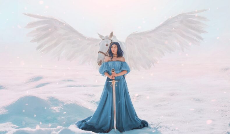 O femeie frumoasă care poartă o rochie albastră vaporoasă în timp ce stă în zăpadă și ține în mâini o sabie și este sprijinită de un cal înaripat pentru a simboliza că este una dintre cele mai puternice femei din zodiac