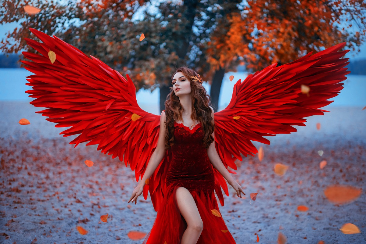 O femeie frumoasă într-un cadru feeric care poartă o rochie roșie cu aripi de înger roșii pentru a demonstra că este una dintre cele mai senzuale femei ale zodiacului