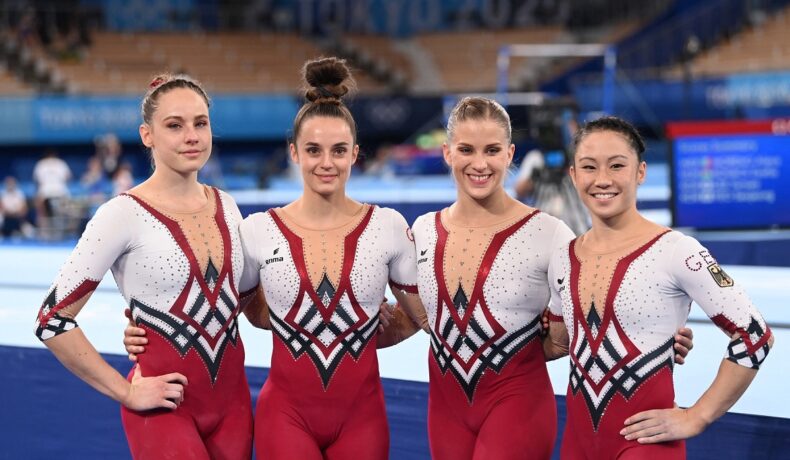 Gimnastele din Germania în timp ce se țin după umăr și poartă costume întregi în culorile alb cu roșu la Jocurile Olimpice de la Tokyo din 2020