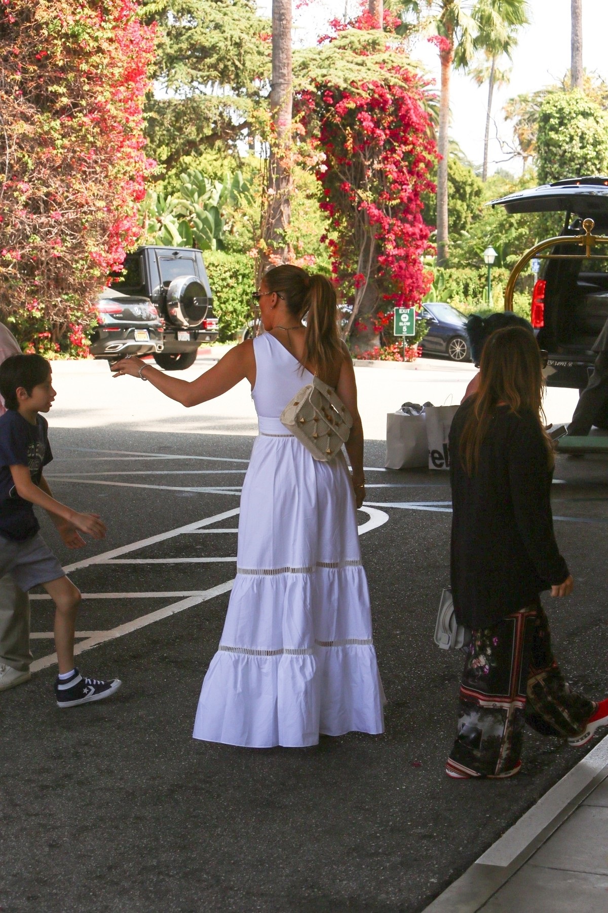 Jennifer Lopez într-o rochie abă pe umăr în timp ce întinde mâna către fiul său Max