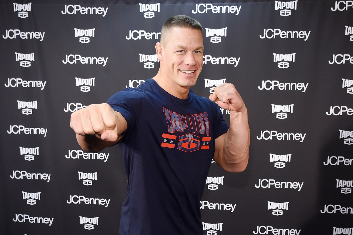John Cena într-un tricou gri în timp ce își ține brațele încordate și arată cu pumnul către public la o conferință de fitness din New Tork din 2017