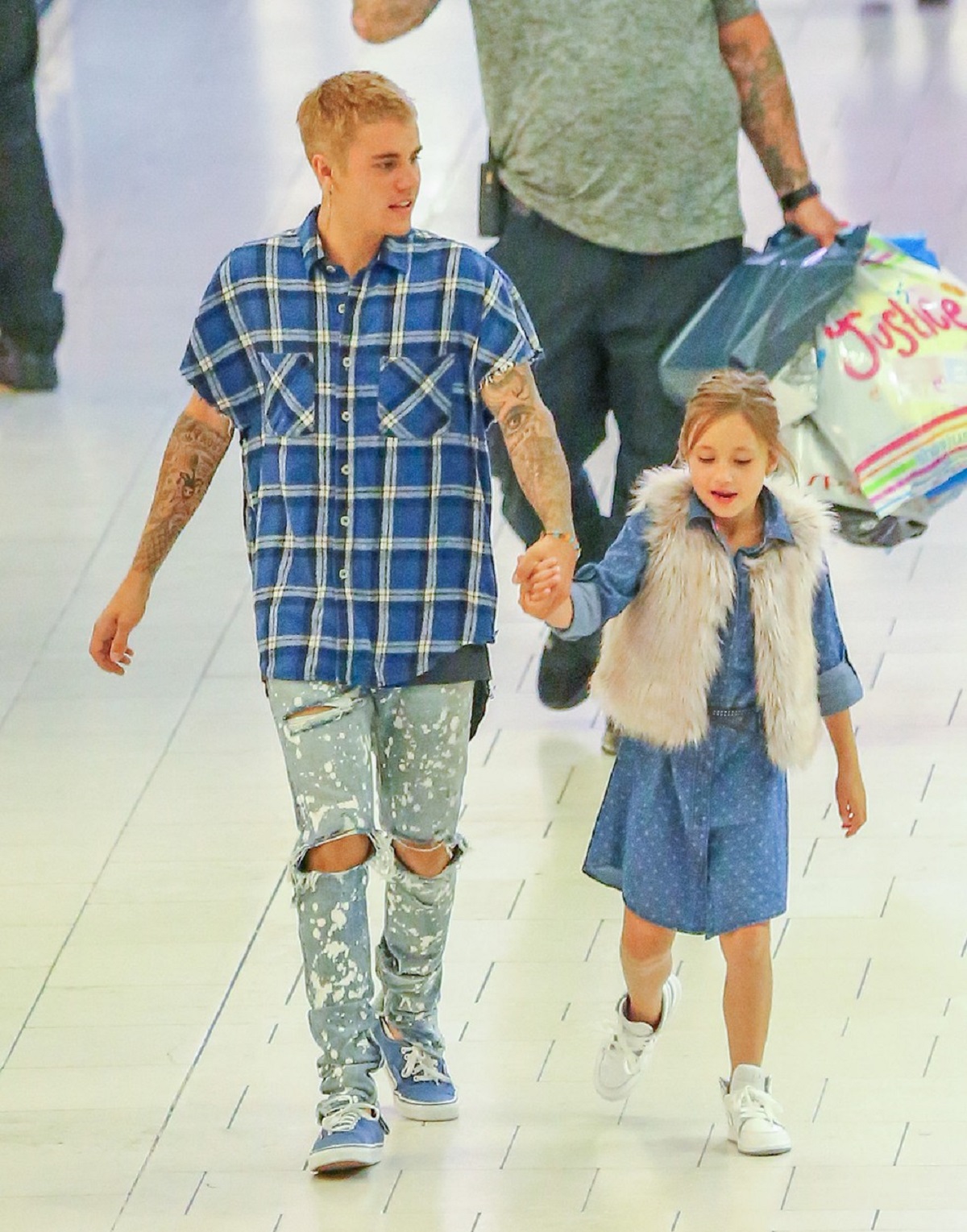Justin Bieber într-o ținută casual cu blugi rupți și o cămașă albastră în carouri în timp ce o ține pe sora lui, Jazmyn de mână la cumpărături în mall