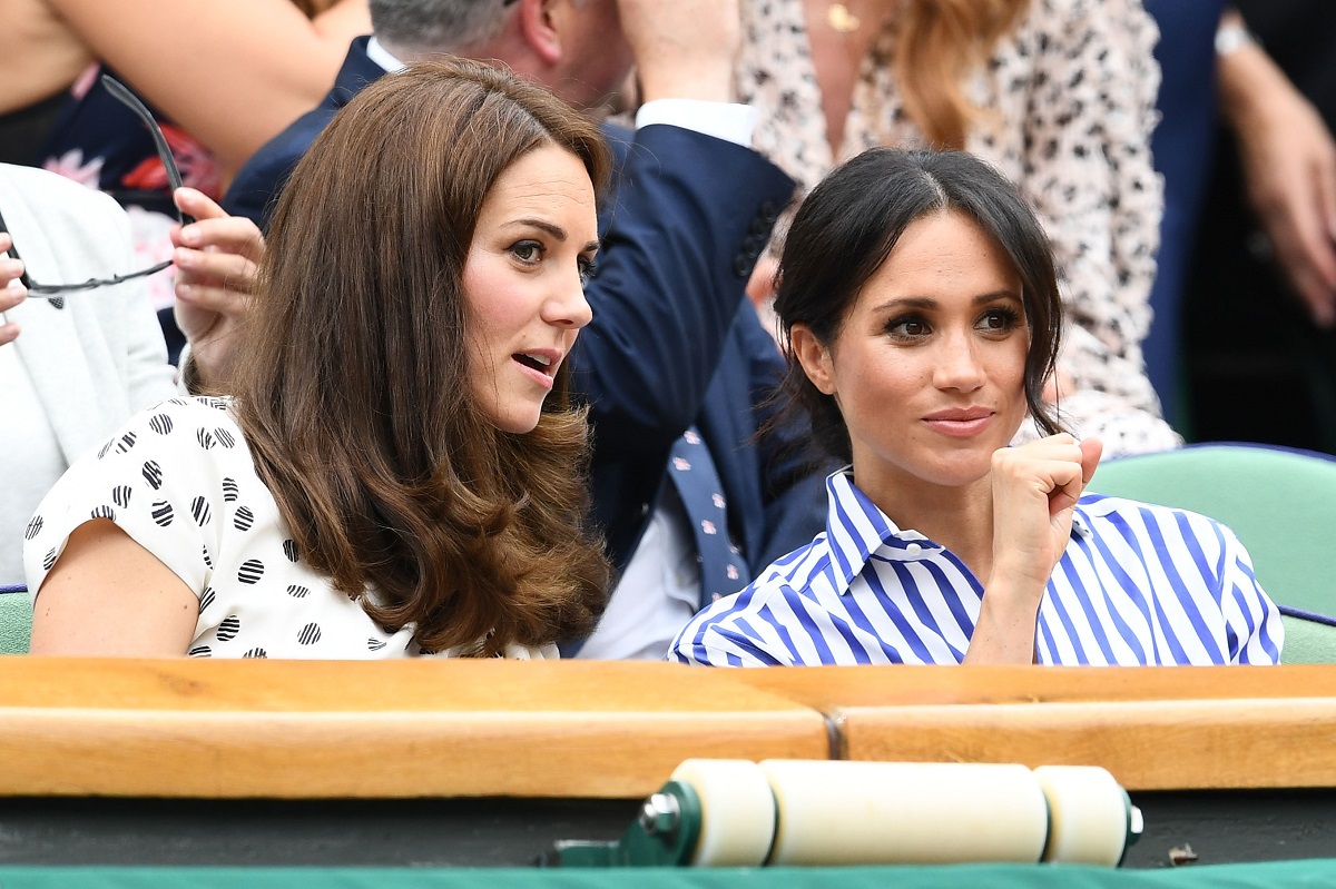 Kate Middleton și Meghan Markle la Turneul Wimbledon în iulie 2018. Cele două au fost surprinsă în timp ce râdeau și glumeau. Kate purta o bluză albă cu buline negre și Meghan purta bluza albă cu dungi albastre