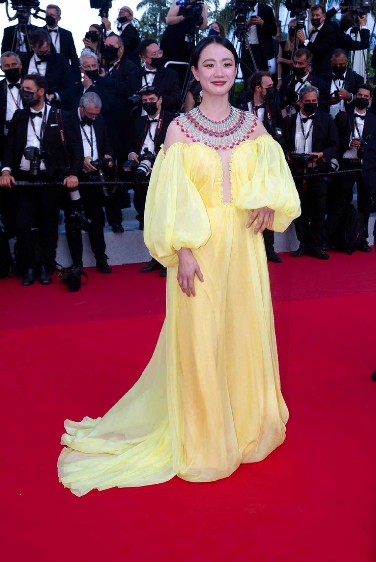 Actrița Meng Li în timp ce pozează pe covorul roșu unde poartă o rochie galbenă cu un colier inspirat din cultura indiană