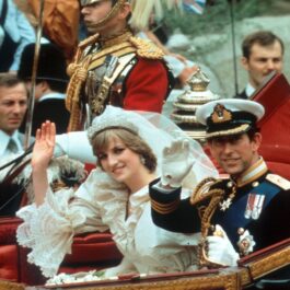 Prințesa Diana în rochie de mireasă alături de Prințul Charles la costum în timp ce fac cu mâna publicului dintr-o trăsură după ce au părăsit catedrala în care s-au căsătorit