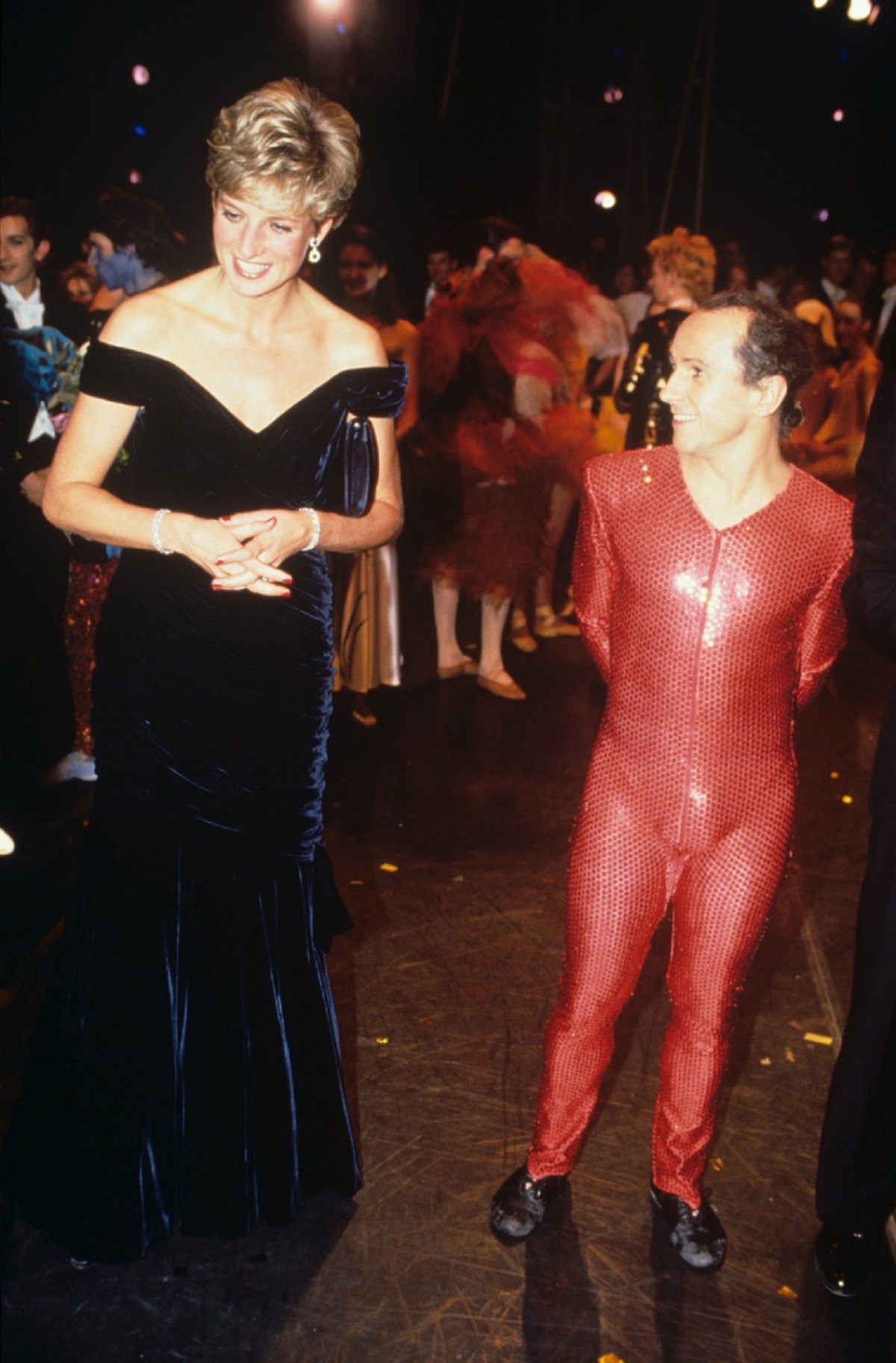 Porfesorul de dans al Prințesei Diana, Wayne Sleep, într-un costum cu paiete roșu alături de Lady Di îmbrăcată într-o rochie elegantă neagră în timp ce vorbesc la Carnavalul Păsărilor din cadrul Casei Regale de Operă în anul 1991