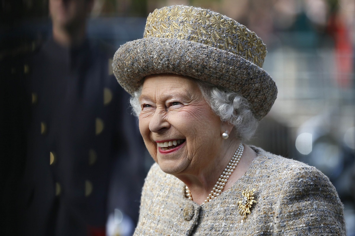 Regina Elisabeta îmbrăcată la costum argintiu cu pălărie în timp ce zâmbește la o întâlnire oficială din Londra în 2014, înainte să se afle că i-ar putea scoate pe Ducii de Sussex de pe lista invitaților la Jubileul de Platină