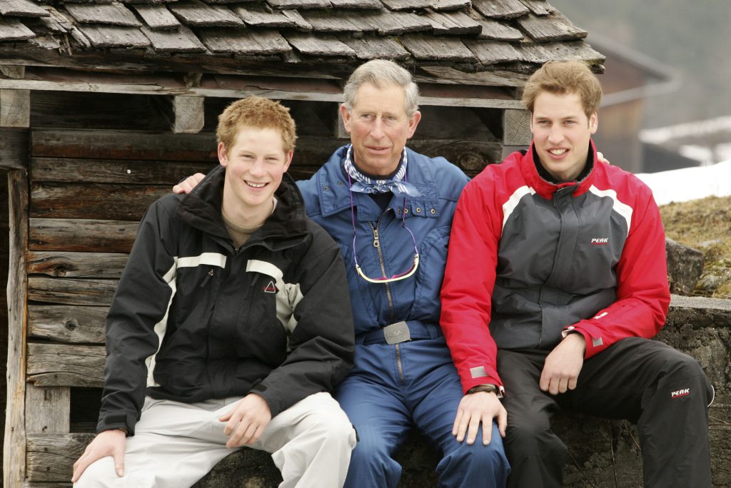Printii Charles, Harry, William, în vacanța de ski din Elveția, Klosters, în 2005. Toți 3 îmbrăcați în costume de ski, cu zăpadă și o cabană în spate