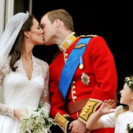 Kate Middleton și prințul William în ziua nunții din anul 2011, sărutul pe balcon după ceremonei. Ea în rochie de mireasă, el în uniforma roșie.