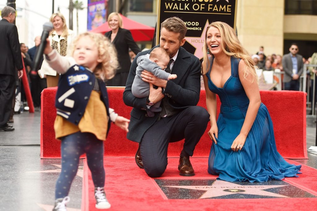 Ryan Reynolds și Blake Lively, plus două dintre fiicele lor, în decembrie 2016, când el a primit o stea pe Hollywood Walk of Fame. Reynolds e îmbrăcat într-un costum negru și Lively poartă o rochie albastră, cu decolteu. Fundalul e roșu