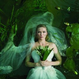 Kirsten Dunst în filmul Melancholia, 2011. E îmbrăcată ca o mireasă, cu un buchet de flori, într-un lac verde, cu nuferi