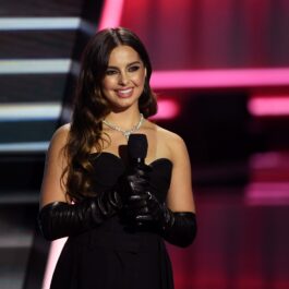 Addison Rae într-o rochie neagră fără bretele și cu mănuși negre în timp ce ține un microfon și se află pe scenă la Billboard Music Awards în 2020