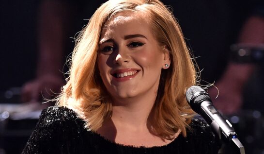 Portret al artistei Adele în timp ce zâmbește și are un față un micorfon la unul din concertele sale