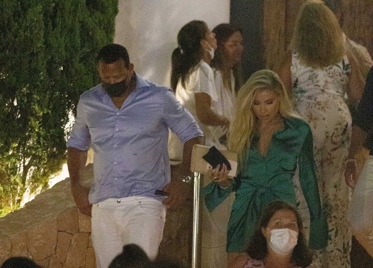 Alex Rogriguez la cămașă în dungi albastre și blugi albi, alături de Melanie Collins într-o rochie verde în timp ce coboară scările și merg la o petrecere în Ibiza