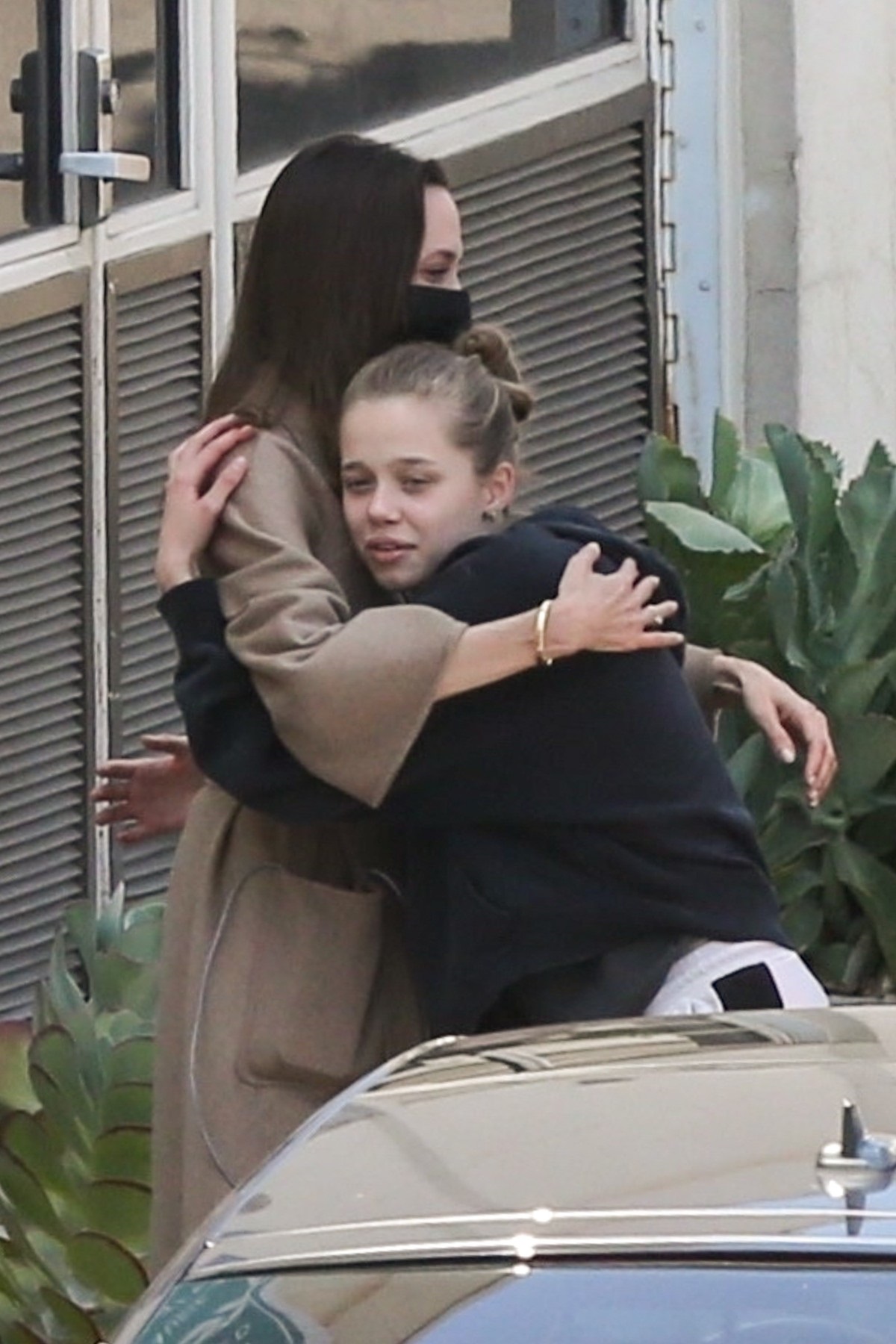 Shiloh Jolie-Pitt într-un hanorac negru în timp ce o strângeîn brațe pe mama sa, Angelina Jolie, care poartă un trench maroniu