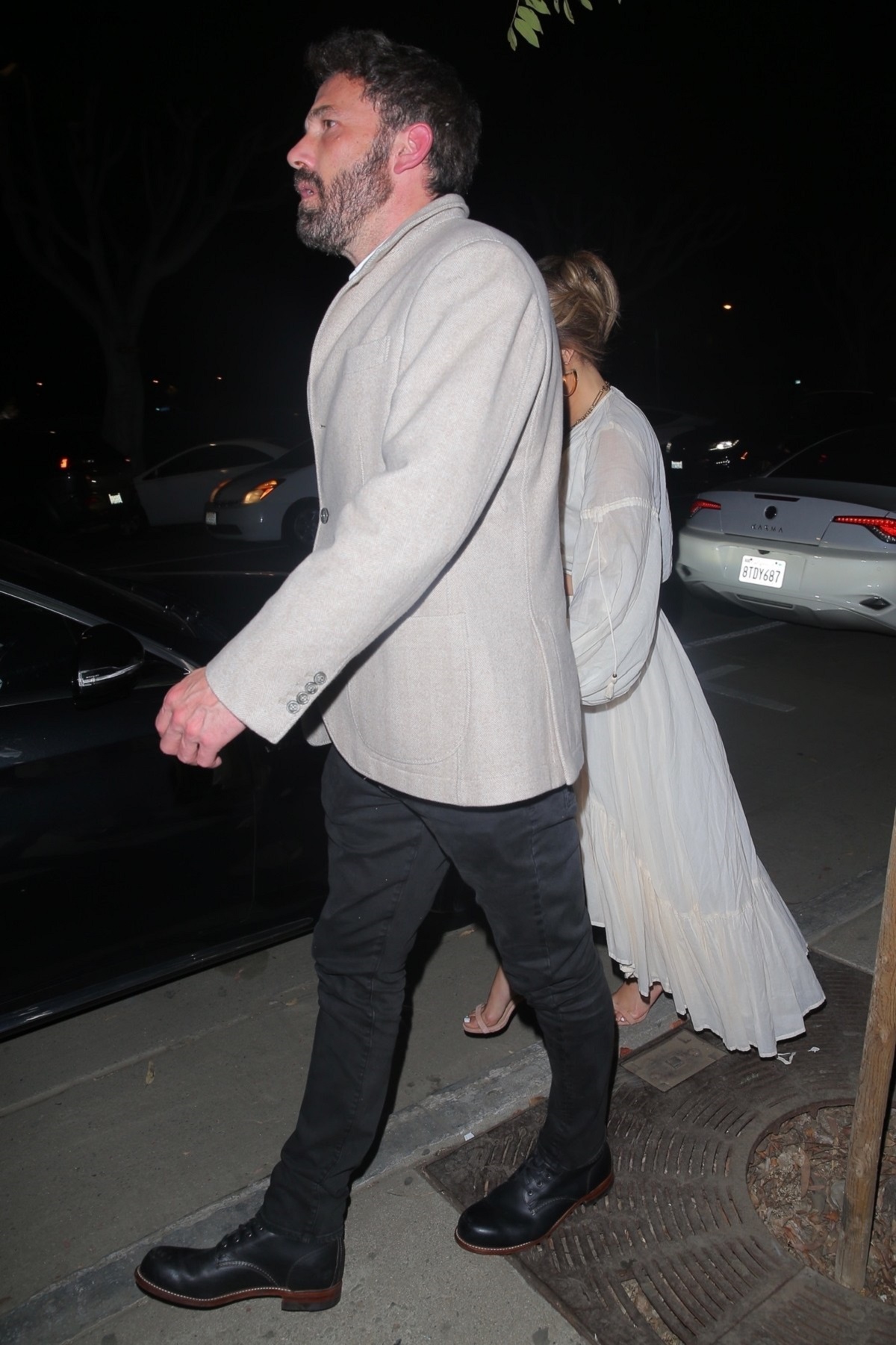 Ben Affleck purtand o pereche de pantaloni negri si un sacou bej în timp ce o conduce pe Jennifer Lopez care poarta o fusta alba transparenta