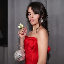 Camila Cabello purtând o rochie roșie fără bretele în timp ce ține în mână o poșetă în formă de sferă cu pietre prețioase