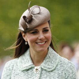 Kate Middleton purtând un sacou alb cu albastru și o pălăriuță specială în timp ce zâmbește