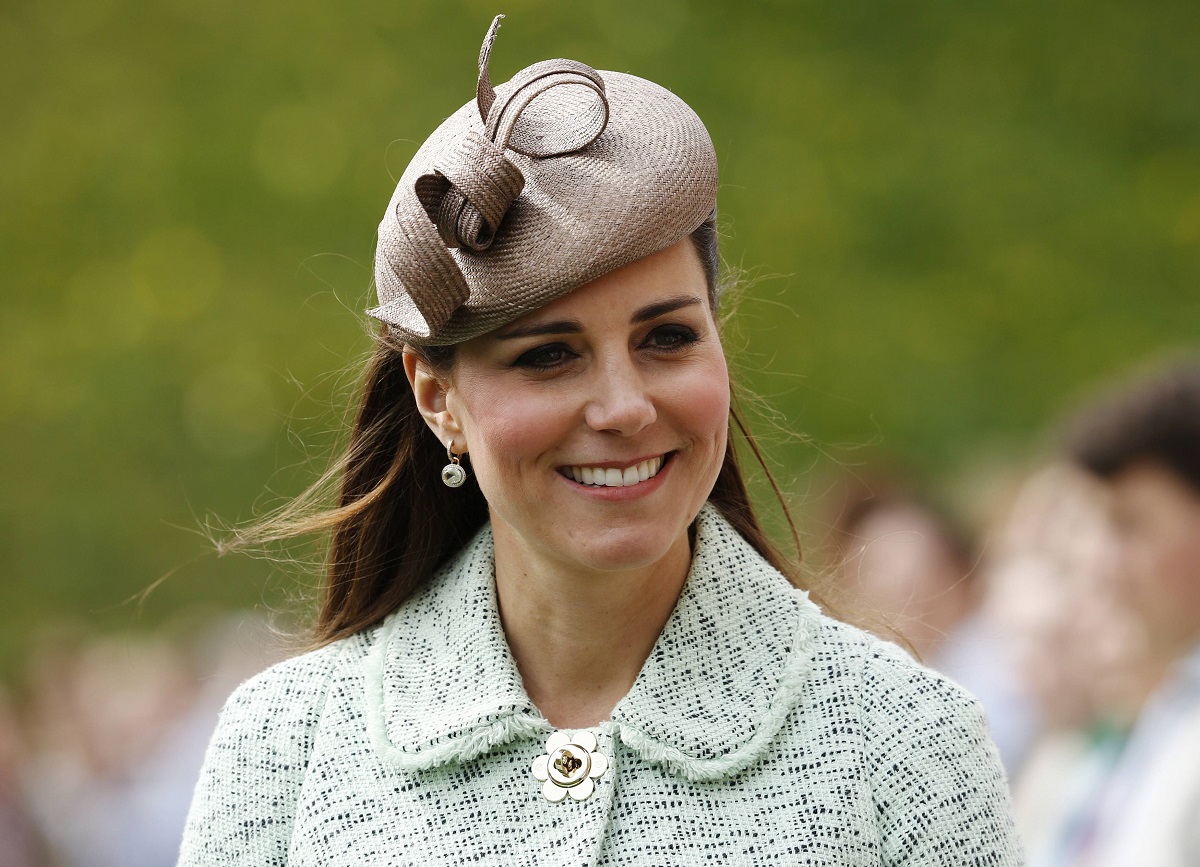 Kate Middleton purtând un sacou alb cu albastru și o pălăriuță specială în timp ce zâmbește