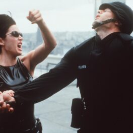 Actrița Carrie-Anne Moss într-o scenă din Matrix în timp ce lovește un polițist cu pumnul în față
