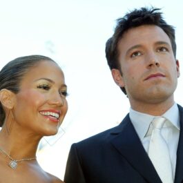 Jennifer Lopez cu părul prins în coc în timp ce zâmbește alături de Ben Affleck care poartă un costum negru cu o cămașă albă