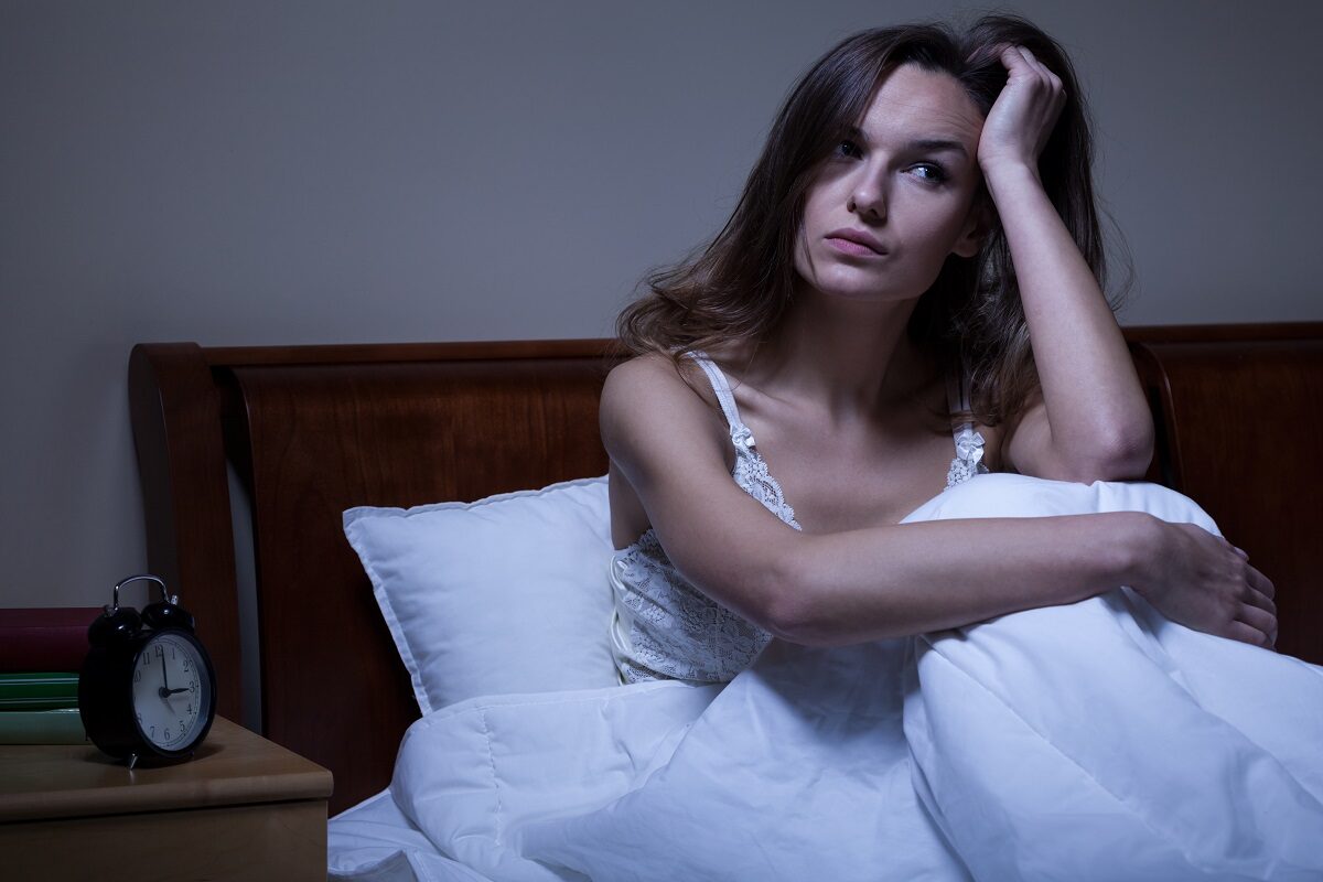O femeie frumoasă care își ține o mână în păr în timp ce stă în pat supărată deaorece s-a trezit din timpul somnului noaptea