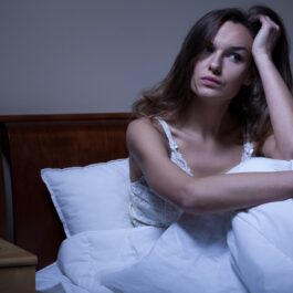 O femeie frumoasă care își ține o mână în păr în timp ce stă în pat supărată deaorece s-a trezit din timpul somnului noaptea