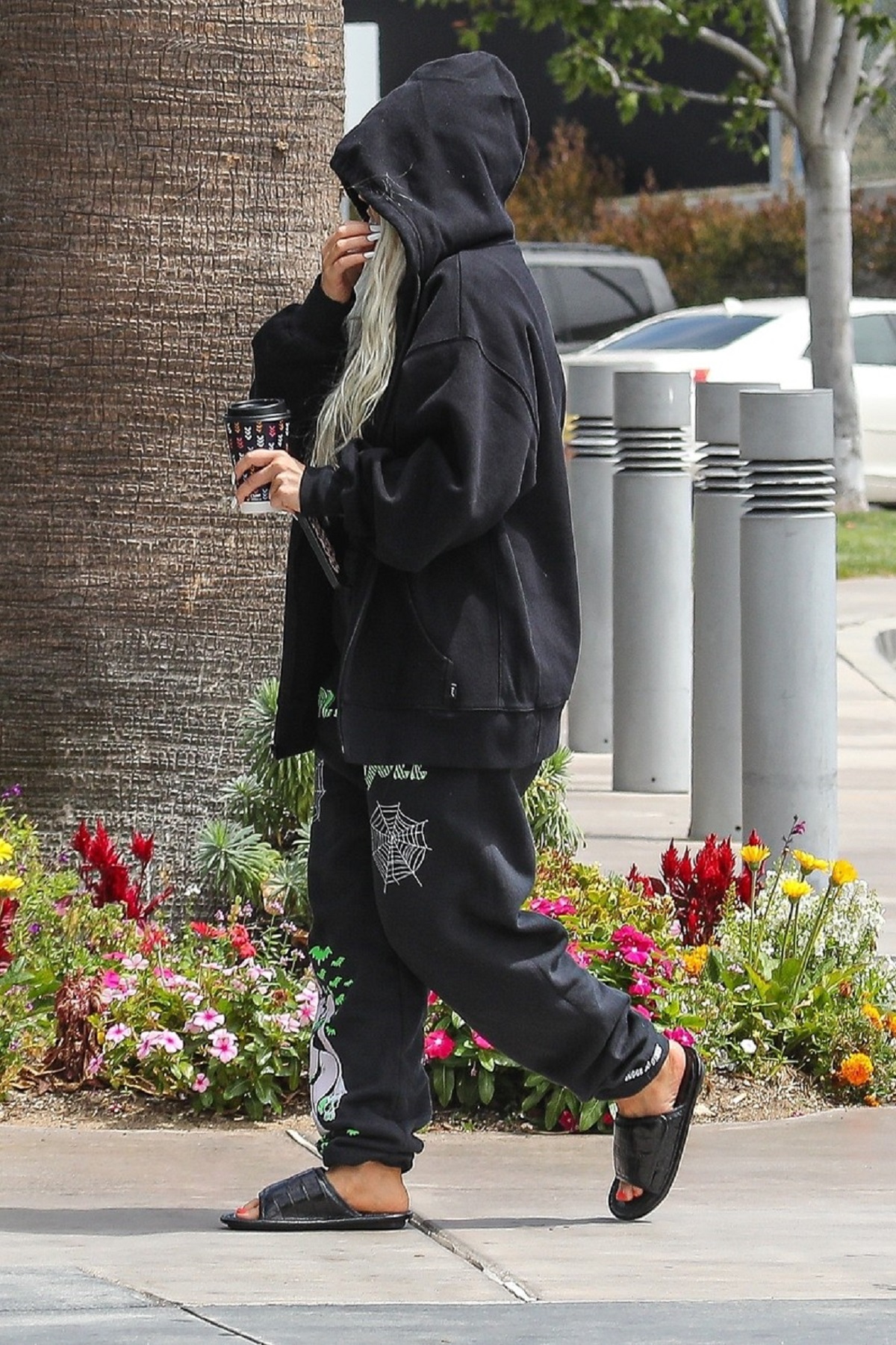 Christina Aguilera purtând un hanorca negru cu glugă, o pereche de pantaloni de trening și papuci în timp ce se îndreaptă către aeroportul din Los Angeles