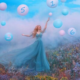 O femeie frumoasă într-o rochie albastră care se află pe o pajiște în timp ce întinde mâna către baloane colorate în roz și albastru pe care se află scrisă cifra destinului