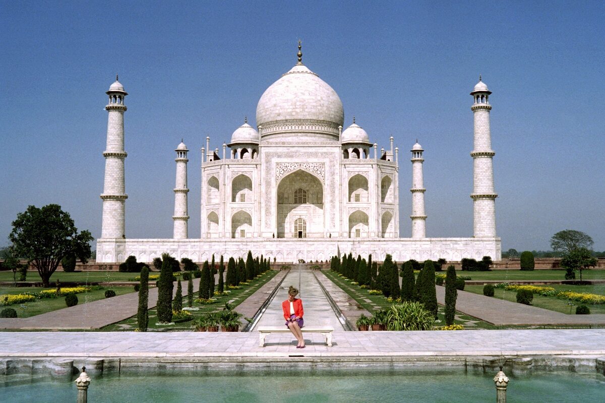 Prințesa Diana într-un sacou roșu și o fustă mov în timp ce stă pe o bancă în fața monumentului de la Taj Mahal