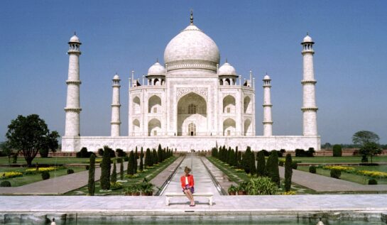 Prințesa Diana într-un sacou roșu și o fustă mov în timp ce stă pe o bancă în fața monumentului de la Taj Mahal