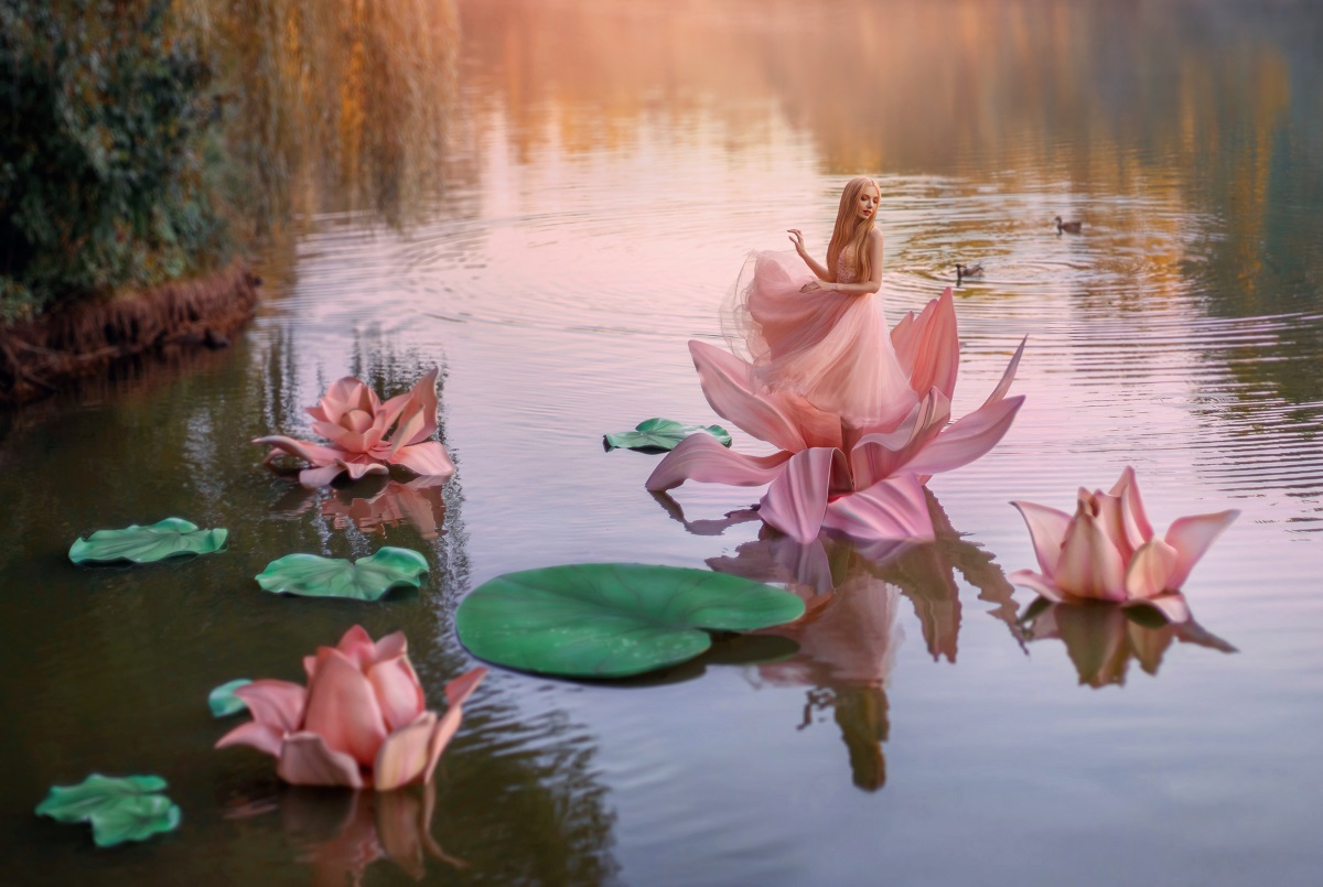 O zână frumoasă într-o rochie roz care dansează pe o floare de nufăr în timp ce seaflă pe un lac umplut cu nuferi și se gândește la acele gesturi pe care zodiile de apă le adoră într-o relație