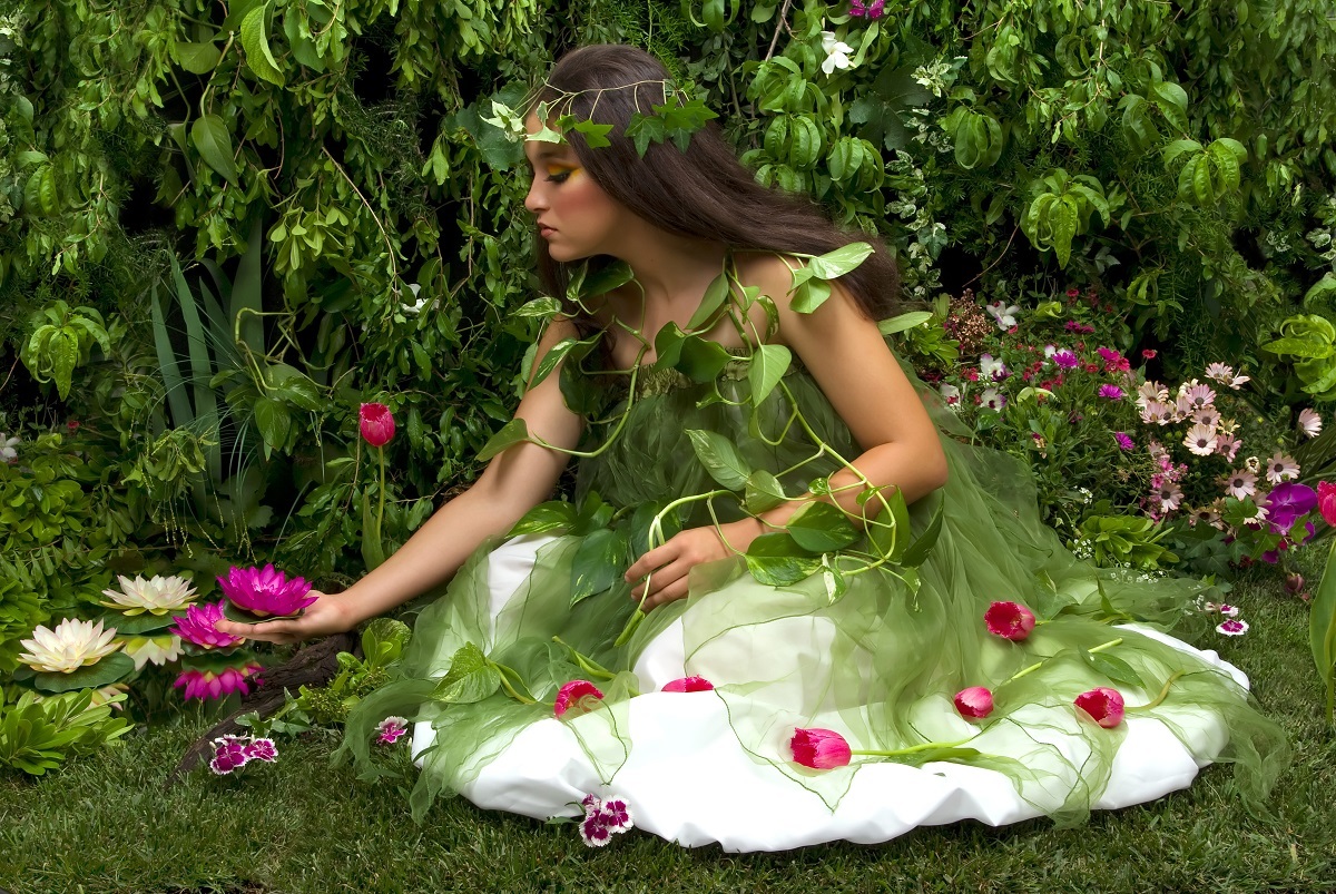 O femeie frumoasă care poartă o rochie albă împodobită cu frunze și flori și care culege flori de nufăr roz pentru a reprezenta acele gesturi pe care zodiile de pământ le adoră într-o relație