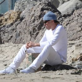 James Haven Voight într-o bluză albă și o pereche de pantaloni mulați albi în timp ce ia prânzul singur pe plajă