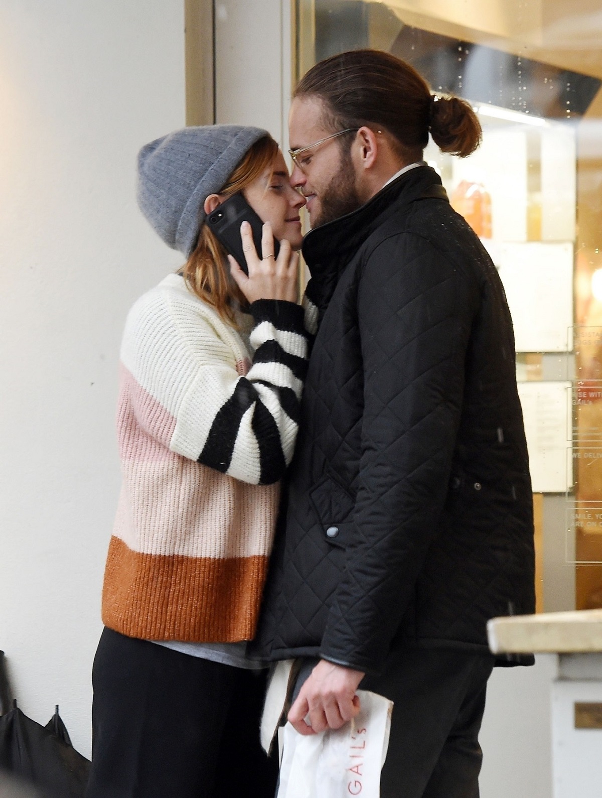 Leo Robinton într-o geacă neagră cu părul prins într-un coc în timp ce o sărută pe frunte pe iubita sa Emma Watson