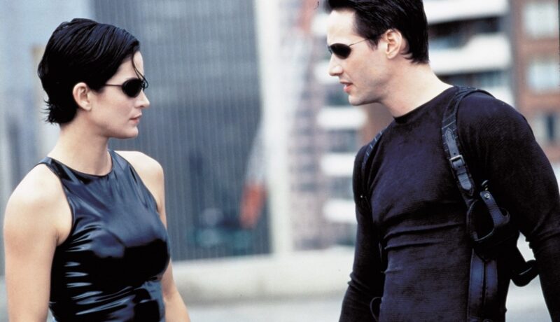 Keanu Reeves și Carrie-Anne Moss îmbrăcați în ținute negre într-o scenă din filmul Matrix din 1999
