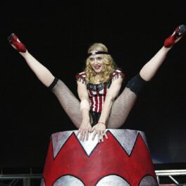 Madonna într-un costum de circ în timp ce face șpagatul pe o trambulină specială colorată cu roșu și alb