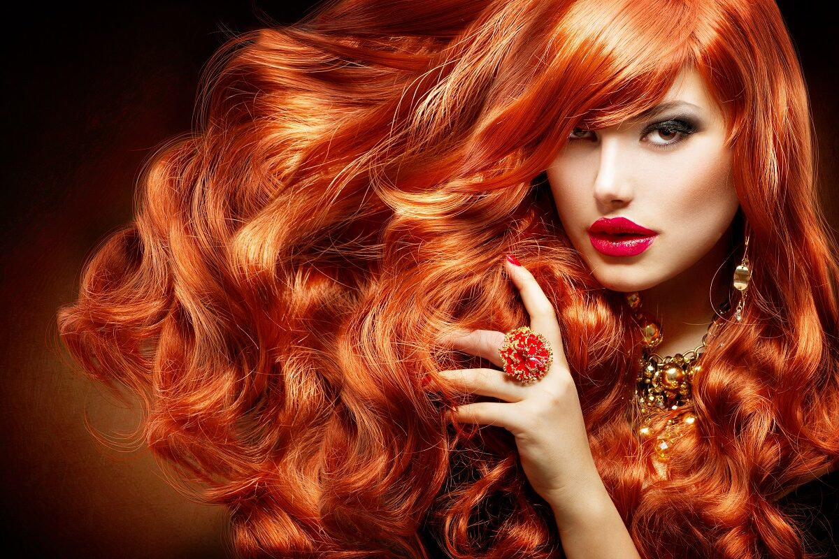 O femeie frumoasă cu un păr superb roșcat în timp ce privește intens la cameră și își trece mâna prin părul creț pe care a folosit una din acele măști naturale pentru părul vopsit