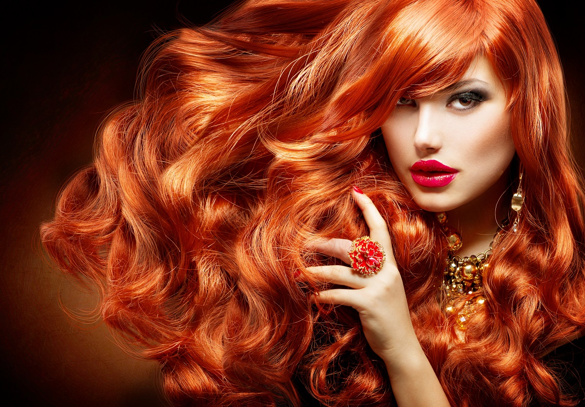 O femeie frumoasă cu un păr superb roșcat în timp ce privește intens la cameră și își trece mâna prin părul creț pe care a folosit una din acele măști naturale pentru părul vopsit