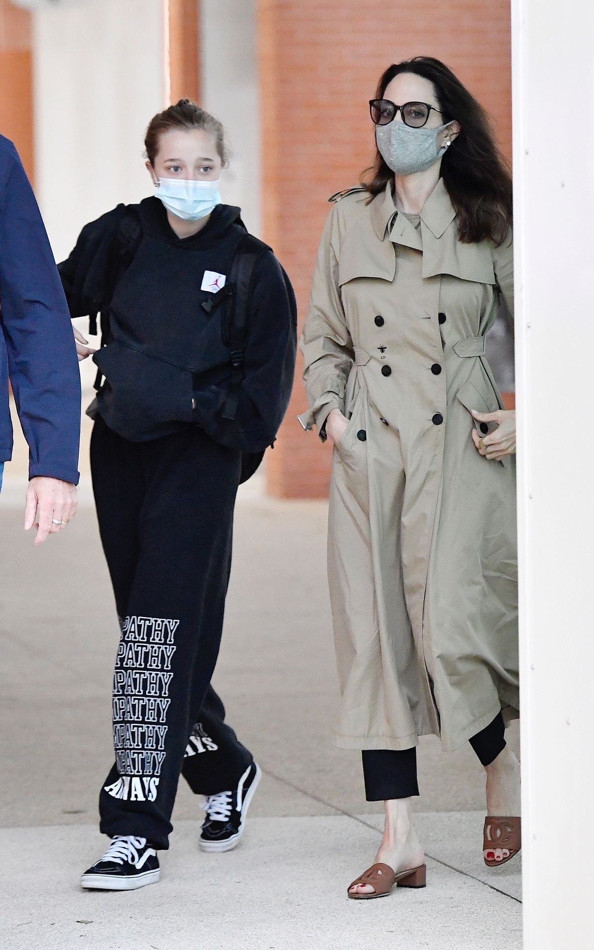 Shiloh Jolie-Pitt îmbrăcată casual în hanorac negru și pantaloni de aceeași culoare, alături de mama sa, Angelina Jolie care poartă un trench crem în timp ce sosesc pe aeroportul din Veneția