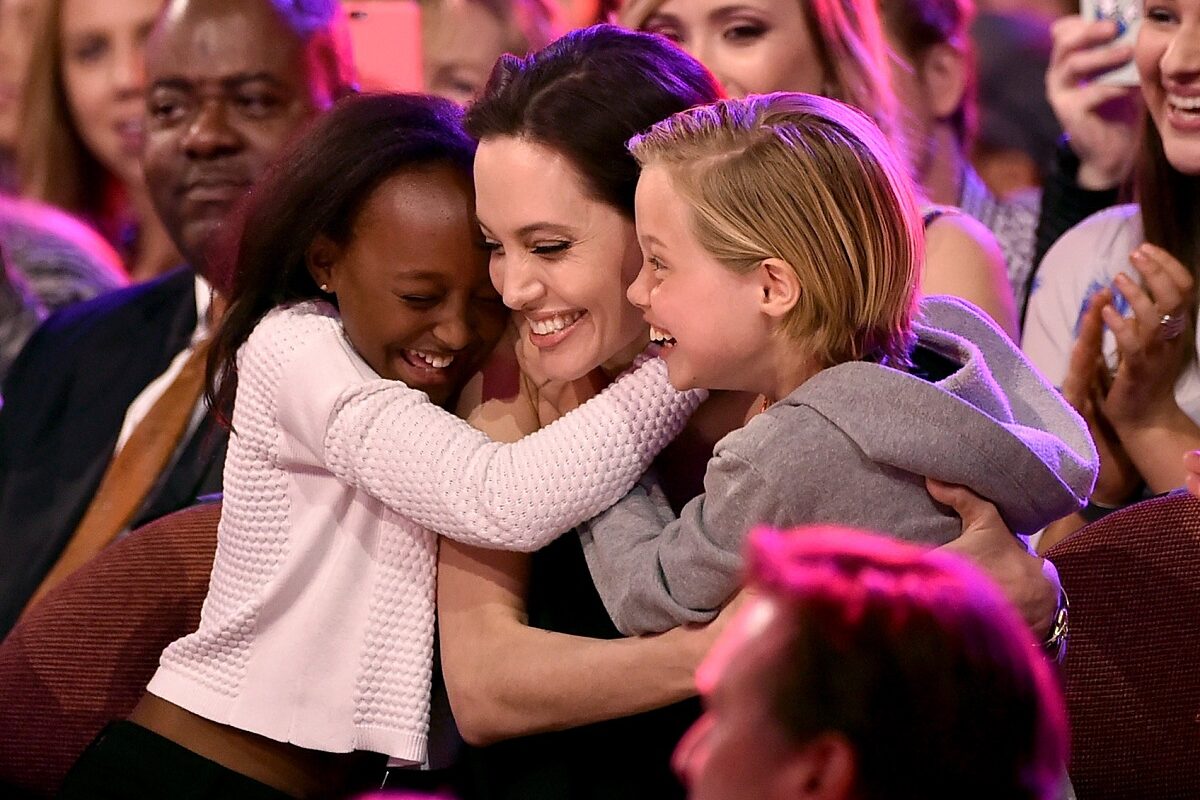 Angelina Jolie într-o rochie neagră în timp ce este îmbrățișată de două dintre fiicele sale, Zahara și Shiloh Jolie-Pitt