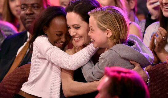 Angelina Jolie într-o rochie neagră în timp ce este îmbrățișată de două dintre fiicele sale, Zahara și Shiloh Jolie-Pitt