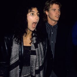 Cher în timp ce strigă și poartă o fustă gri, o bluză neagră și un fular gri cu negru, alături de fostul său iubit Val Kilmer în anul 1984
