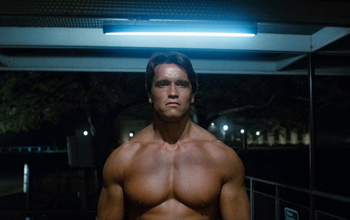 Arnold Schwarzenegger în filmul Terminator. La bustul gol, fundalul cu negru și albastru, din anul 1984
