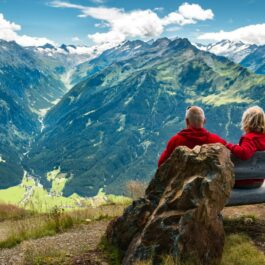 Un cuplu senior stă pe o bancă în Alpii austrieci și demonstează că bătrânețea este o etapă fericită a vieții