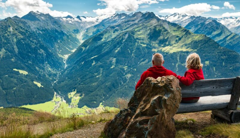 Un cuplu senior stă pe o bancă în Alpii austrieci și demonstează că bătrânețea este o etapă fericită a vieții